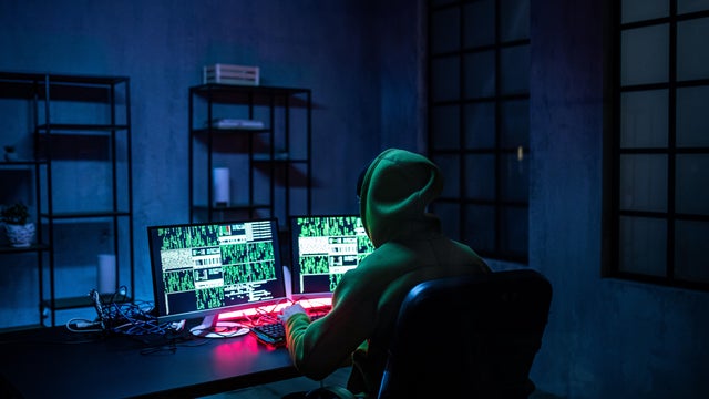 Hacker man working on computers in dark room, rear view. 