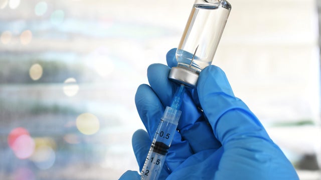 Hand holding syringe inserted in vaccine vial 