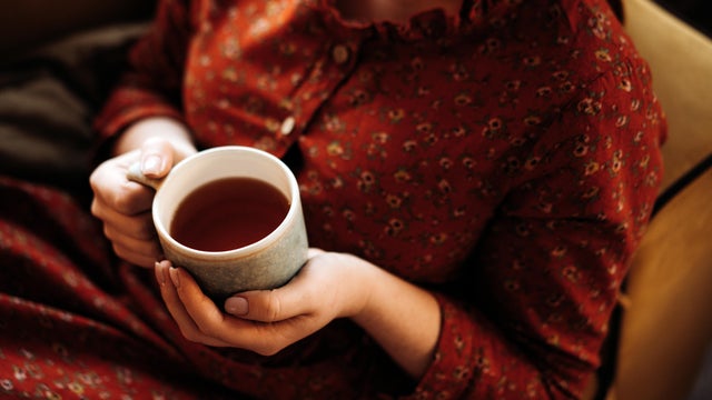 Portrait of a long-haired red-haired woman sitting on the sofa with cup of tea 