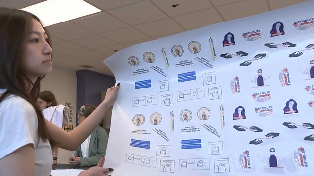 A student holds up a big sheet of stickers from the program 