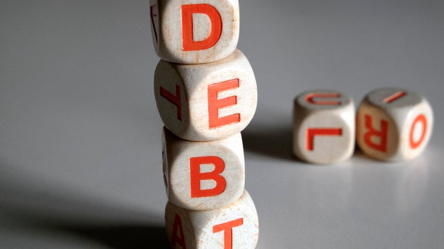White and orange scrabble dice spelling the word "DEBT" 