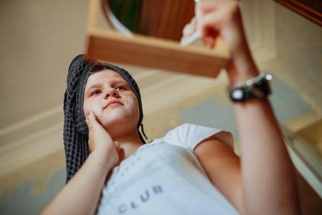 Teenage girl doing her skincare routine looking in the mirror