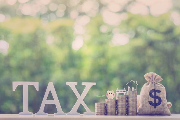 Understanding the Impact of Taxes on Savings and Investments: The word TAX displayed alongside stacks of coins with several icons on top e.g. a piggy bank, a sprouting plant, a car and a family house.