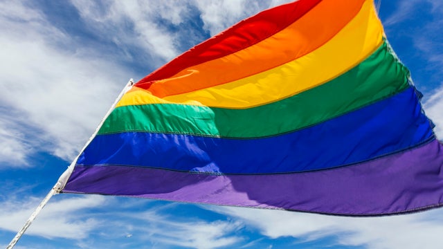 Rainbow flag waiving in the wind against blue sky 