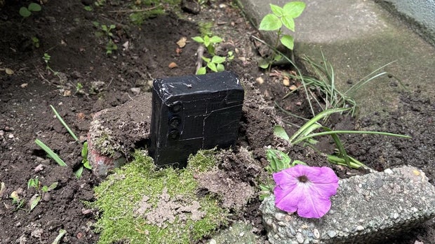 What appears to be an Android phone covered in black tape buried in a yard 