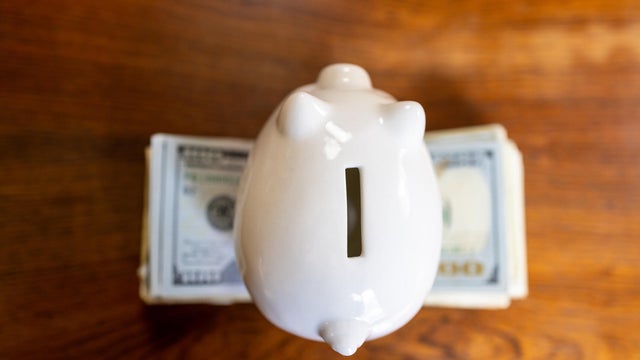 white piggy bank on top of stack of u.s. paper bills 