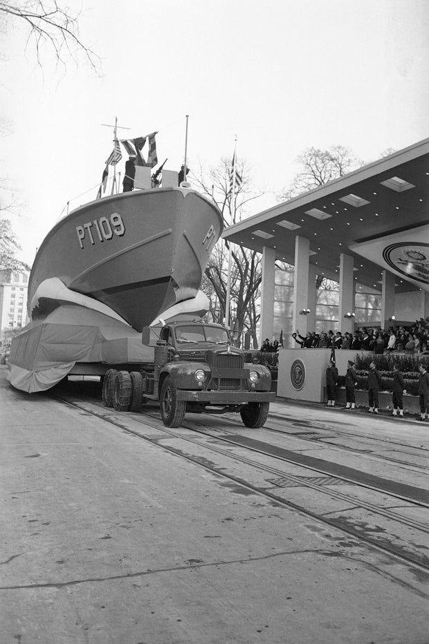 A Navy PT boat rides high above Pennsylvania Avenue on January 20, 1961 as the inaugural parade passes the presidential reviewing stand. President John Kennedy waves to sailors aboard.