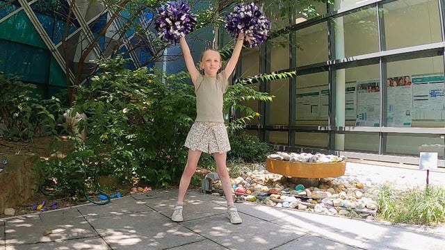 Sadie stands with her arms in the air holding pom poms 