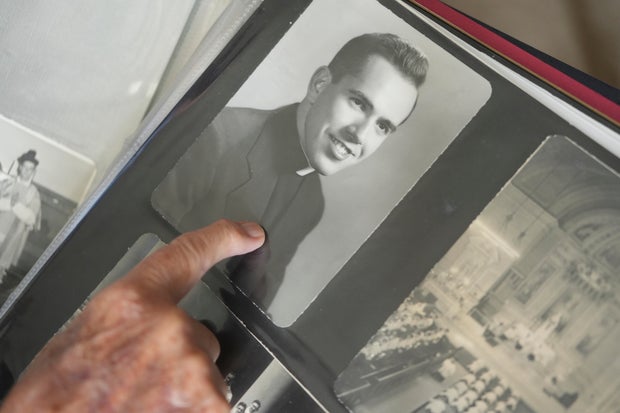 The Rev. James Kelly points to a portrait of himself as a young priest in his photo album during an interview 
