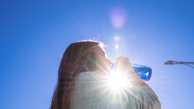 Blonde woman drinking water outside while being illuminated by a ray of sunlight. 