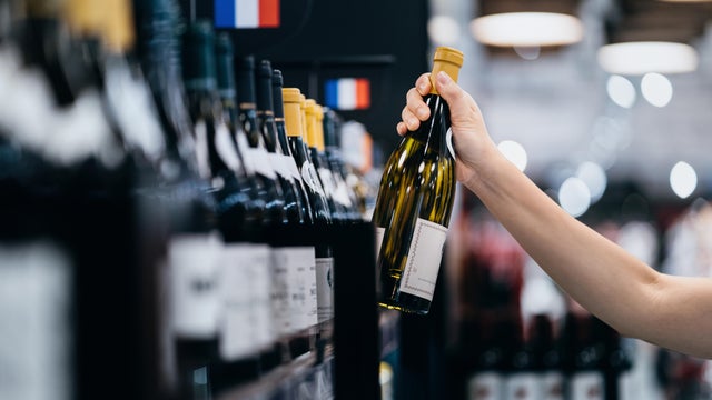 Close-up shot of a young woman choosing wine and picking out a bottle of white whine from the shelf in a liquor store. Grocery shopping. Retail and consumerism 