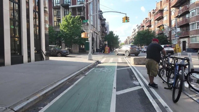 A protected bike lane on Bedford Avenue in Brooklyn separates cyclists from traffic with a row of parked cars. 