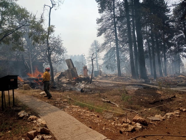 A firefighter stands near smoldering debris and active flames amid the charred remains of burned structures near the Grand Canyon Lodge. 