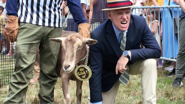 Major League Eating Chair George Shea poses with a goat wearing a chain with a medallion that reads "G.O.A.T." 