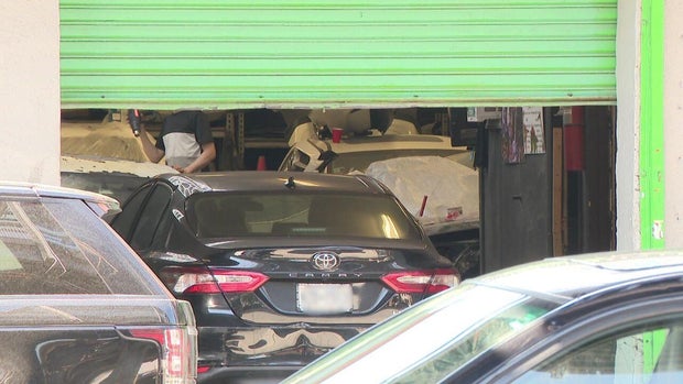 An individual applying a heat gun to a car inside an auto repair shop. 