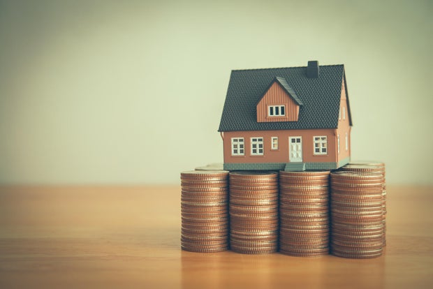 House on heap stack coins on wooden table white wall background copy space. 