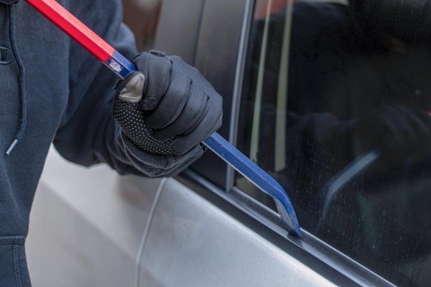 A robber dressed in black holding crowbar at a driver in a car. Car thief concept. 
