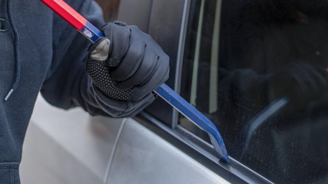 A robber dressed in black holding crowbar at a driver in a car. Car thief concept. 