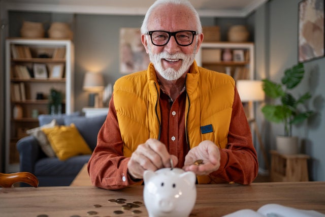 Senior man saving money using piggy bank at home 