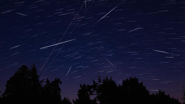 Milky Way stars with meteor shower trails and countryside silhouettes. 