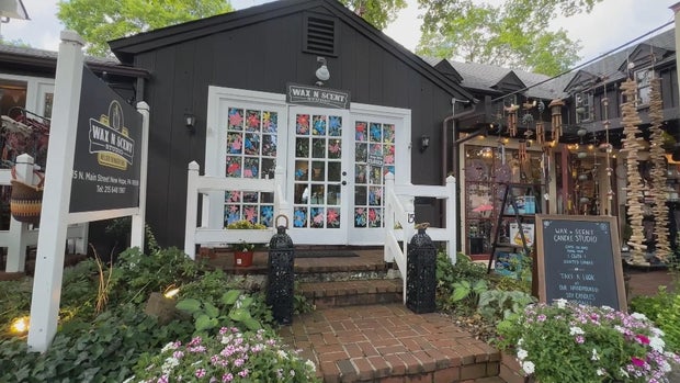 Exterior photo of Wax N Scent Studio, it's a black building with white trim, colorful decorations in the windows 