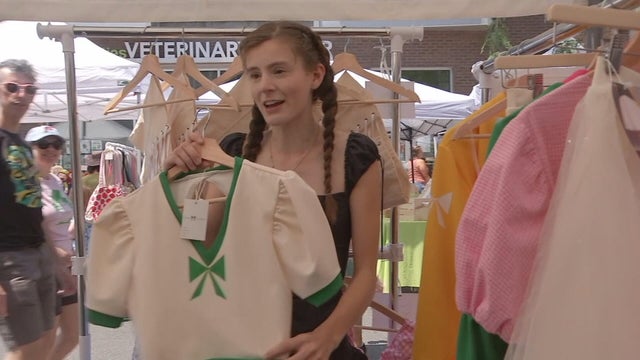 Clothing designer Quinn Caroline holds up a green and cream shirt 