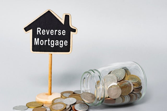 Reverse Mortgage text on wooden house model with coins in a glass jar. 