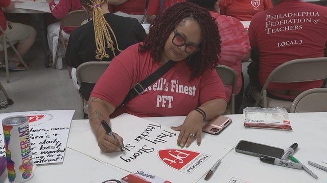 A woman works on a poster with the Philadelphia Federation of Teachers logo that says Philly strong. 