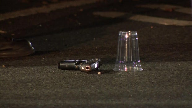 A gun laying in the street next to a cup being used as an evidence marker 