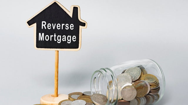 Reverse Mortgage text on wooden house model with coins in a glass jar. 