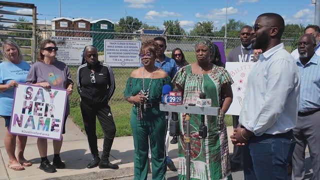 Family of Fanta Bility gather for a memorial event, one has a poster that says Say her name 