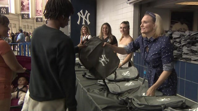 A worker hands an individual a backpack with the Yankees logo on it. 