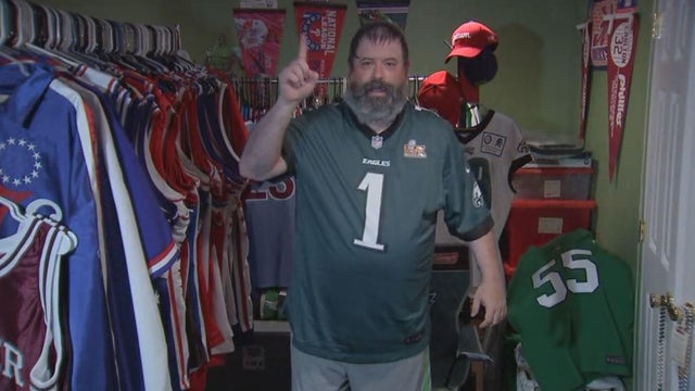 Neil Beck wears a Jalen Hurts jersey in his man cave, holds up No. 1 on his finger 
