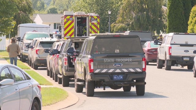 Several state police vehicles and other law enforcement vehicles are seen on a residential street 