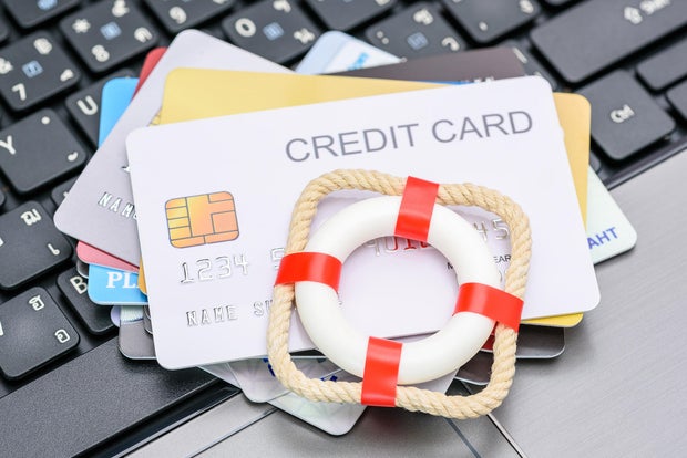  Red lifebuoy or lifebelt atop a stack of credit cards on a laptop, depicting problems in repaying credit card debt. 