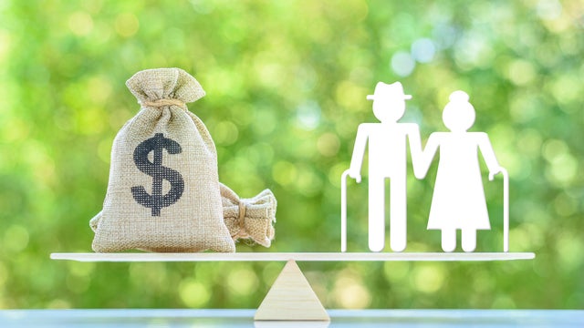 Financial Planning for Seniors : Balancing Retirement Income and Expenses. A miniature elder couple standing on a basic balance scale with US dollar money bag. Elderly face challenges in retirement. 