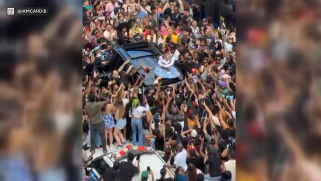 Cardi B sits on the roof of an SUV surrounded by fans 