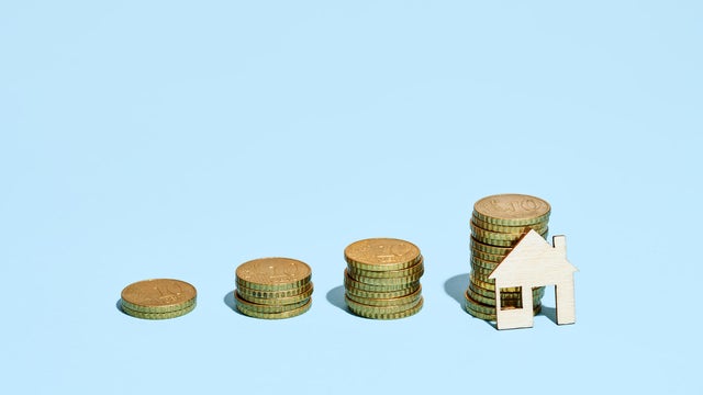 Wooden House Resting On A Stack Of European Union Coins Simulating A Growing Bar Graph 