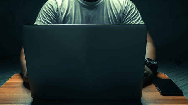 A man in a white shirt sits on a laptop in a dark room. with light shining down. internet concept addiction.topview. 