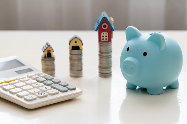 Mini house on stack of coins. Piggy bank and stacked coins on white wooden table. Property investment and house mortgage financial concept