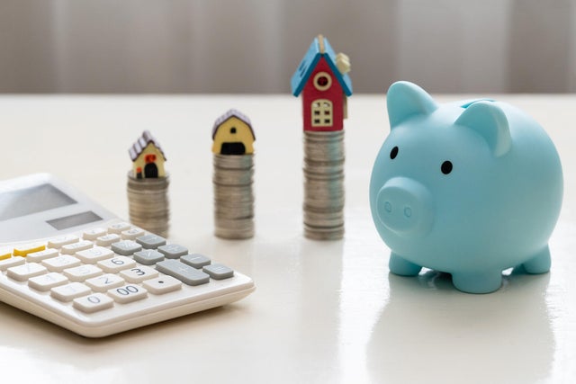 Mini house on stack of coins. Piggy bank and stacked coins on white wooden table. Property investment and house mortgage financial concept 