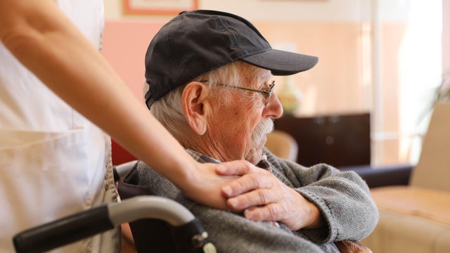 Elderly Man in a Wheelchair Talking to a Nurse at a Nursing Home 