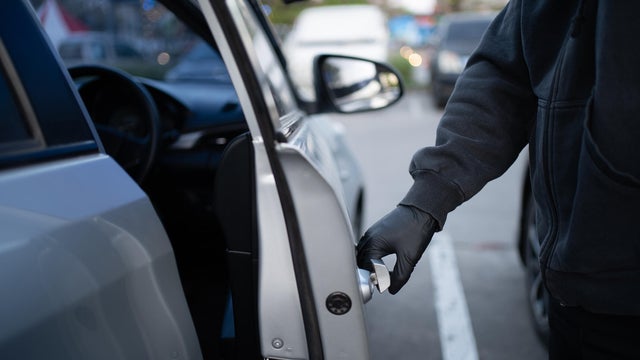 Close-up shot of a thief wearing a black shirt and black gloves opening the car door and trying to break in. Car theft concept generic photo. 