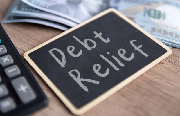 A blackboard with Debt Relief written in chalk, a calculator and US dollar bills. 