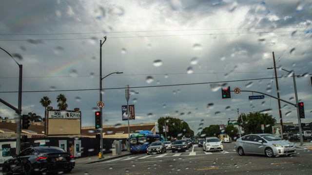 A pedestrian crosses the street in the rain with a view of the The Sixth Street Viaduct 