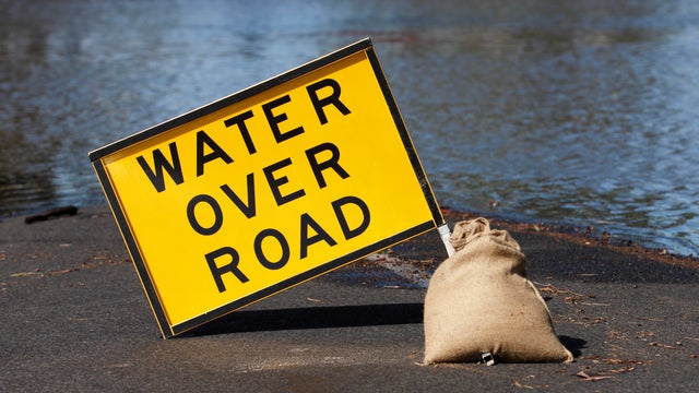 Yellow "Water Over Road" hazard sign and flooded street 
