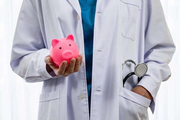 Doctor holding piggy bank in financial insurance concept in hospital