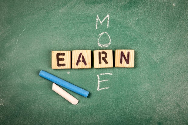 EARN MORE. Wooden alphabet letters on a green chalk board