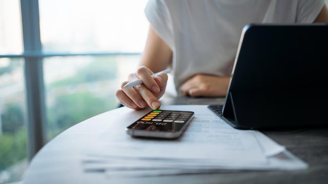 Asian woman managing personal banking and finance. Paying bills online. Making financial plans. Planning budget and calculating expenses with digital tablet while going through bills at home. Home finances. Home budgeting. Banking and finance concept 