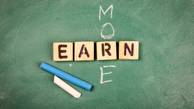 EARN MORE. Wooden alphabet letters on a green chalk board 
